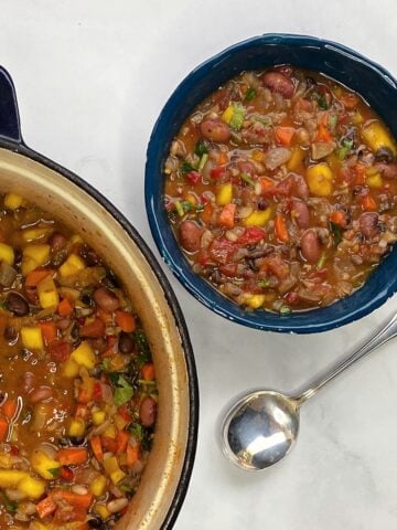 Bowl of mango chili with a spoon to the side. Corner of Dutch oven filled with cooked chili in view.