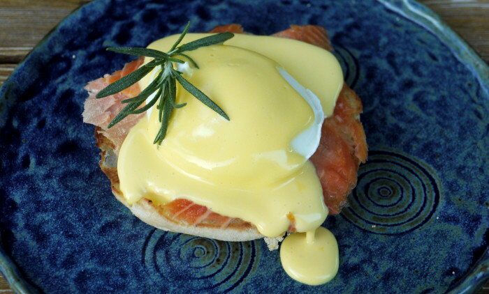 45-degree shot of hollandaise sauce over a salmon Benedict, garnished with a sprig of fresh rosemary. 