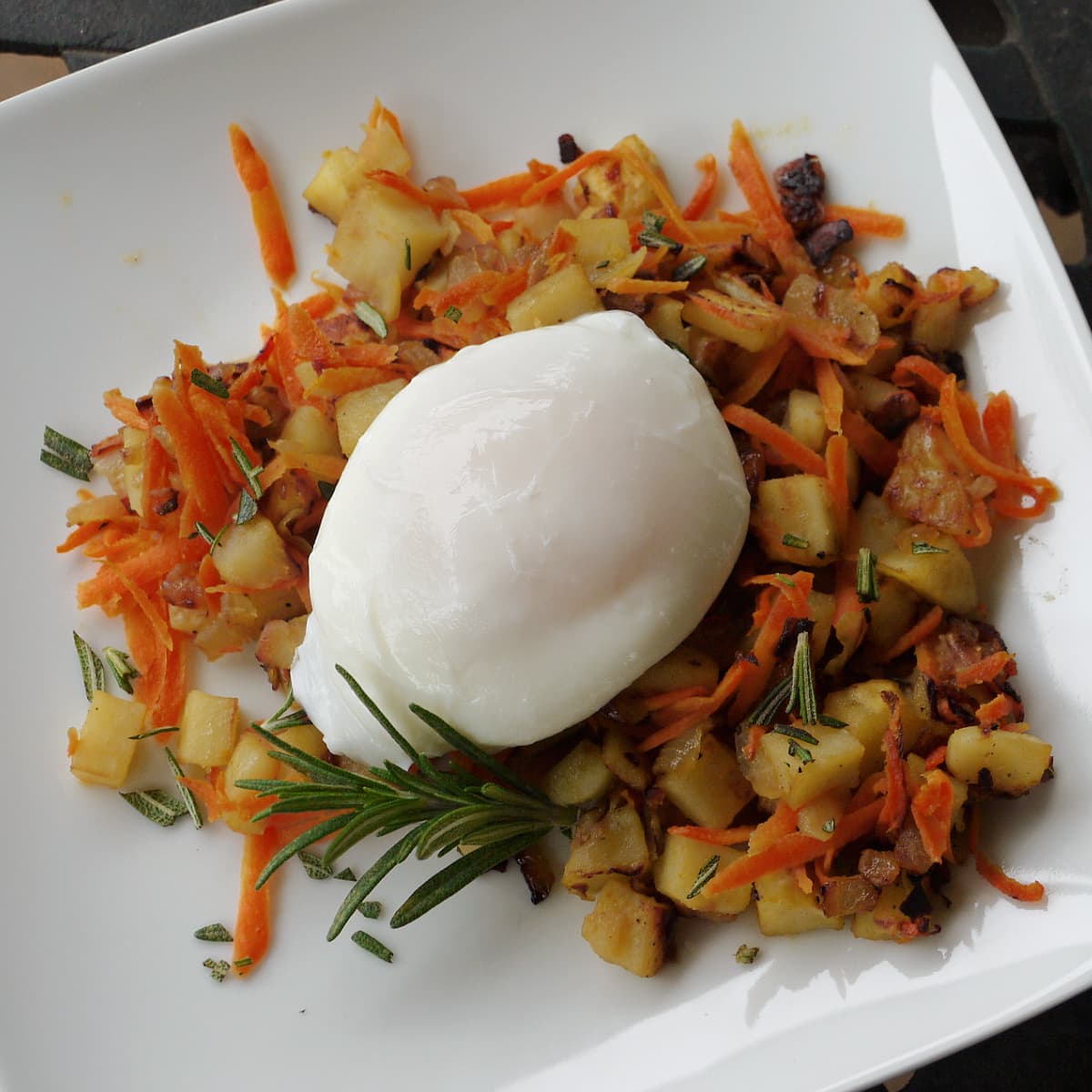 One poached egg sitting atop a small bed of sweet potato hash. Garnished with rosemary.