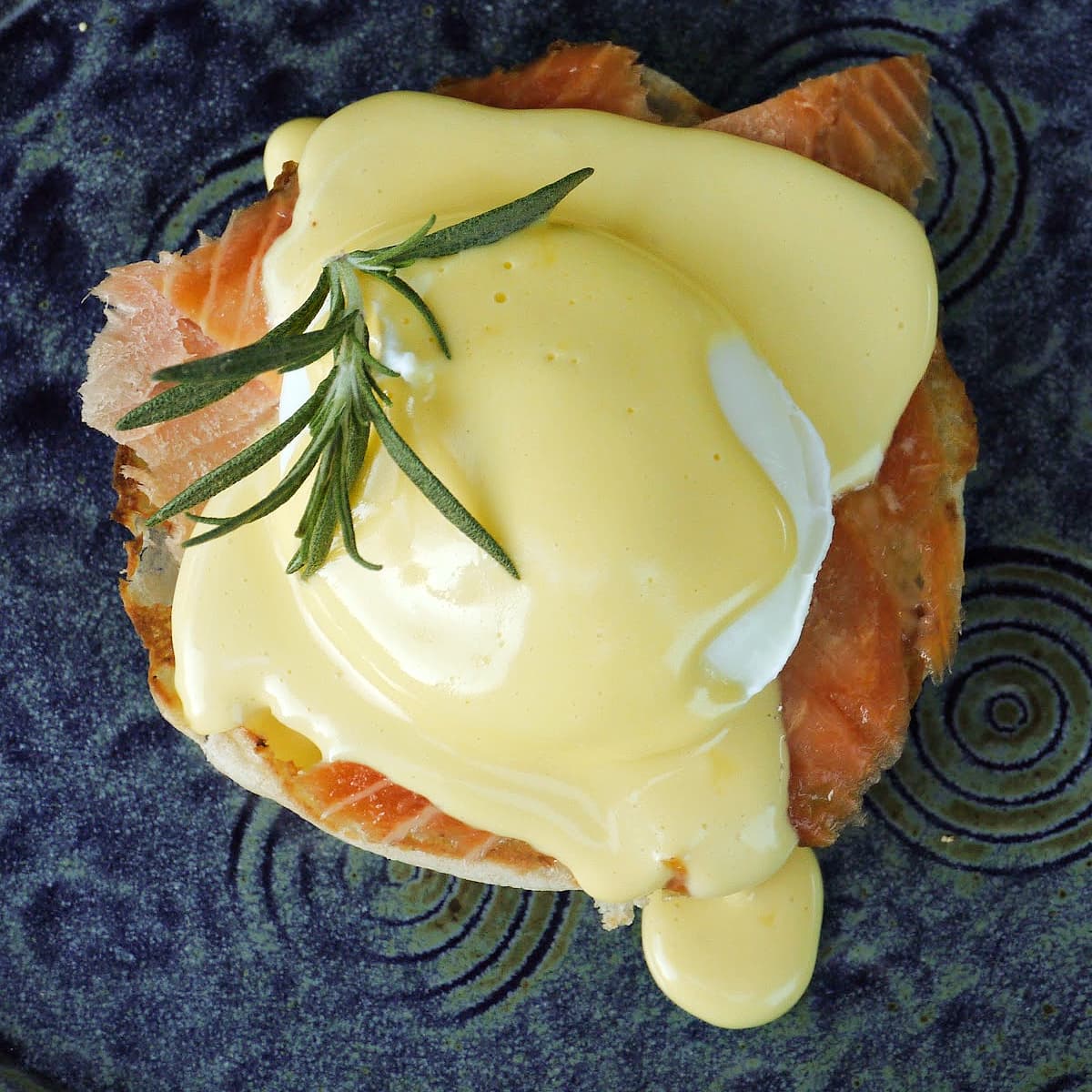 Overhead shot of salmon eggs Benedict, with hollandaise poured over top, garnished with fresh herbs.