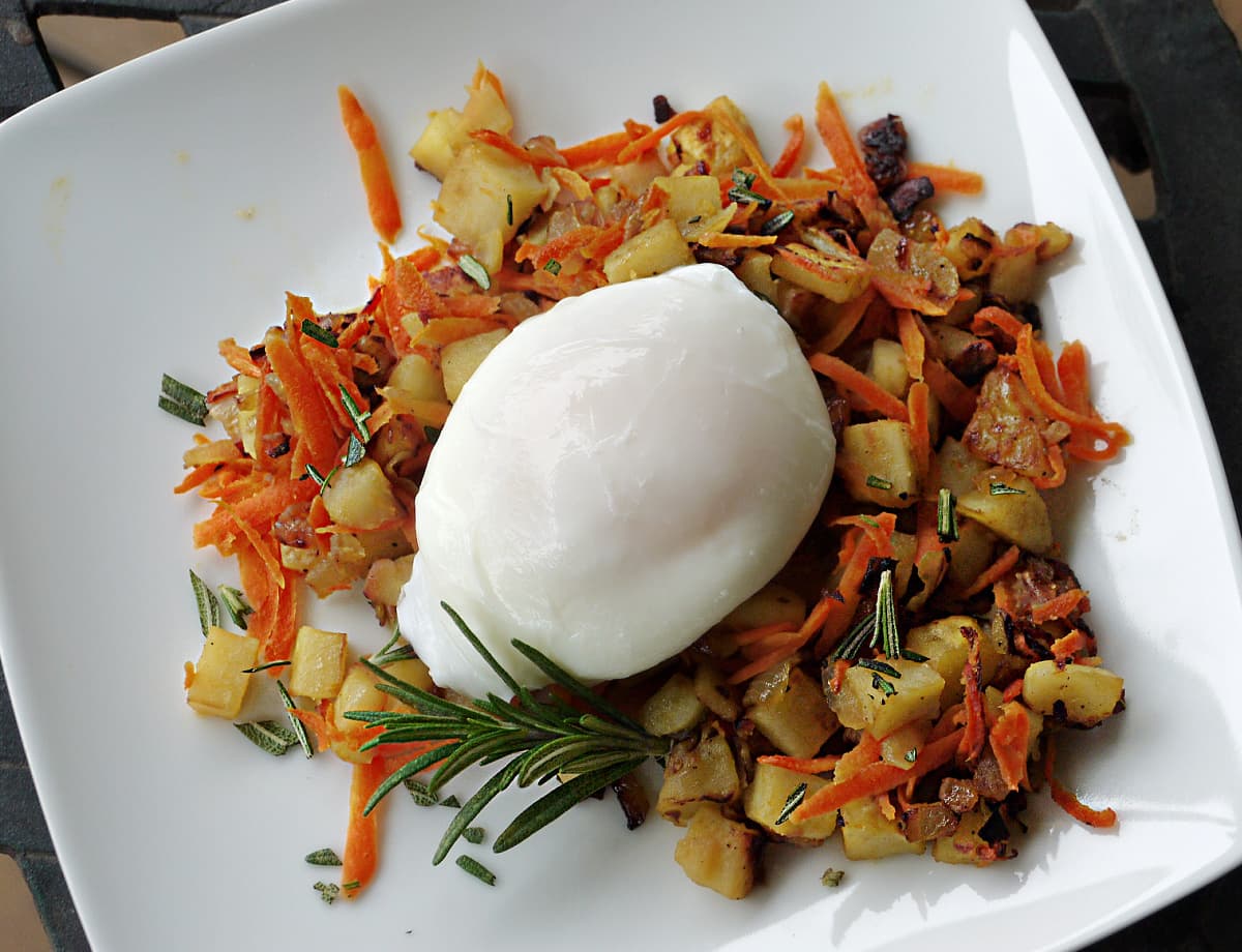 Overhead shot of carrot and sweet potato hash, with an unbroken poached egg on top.