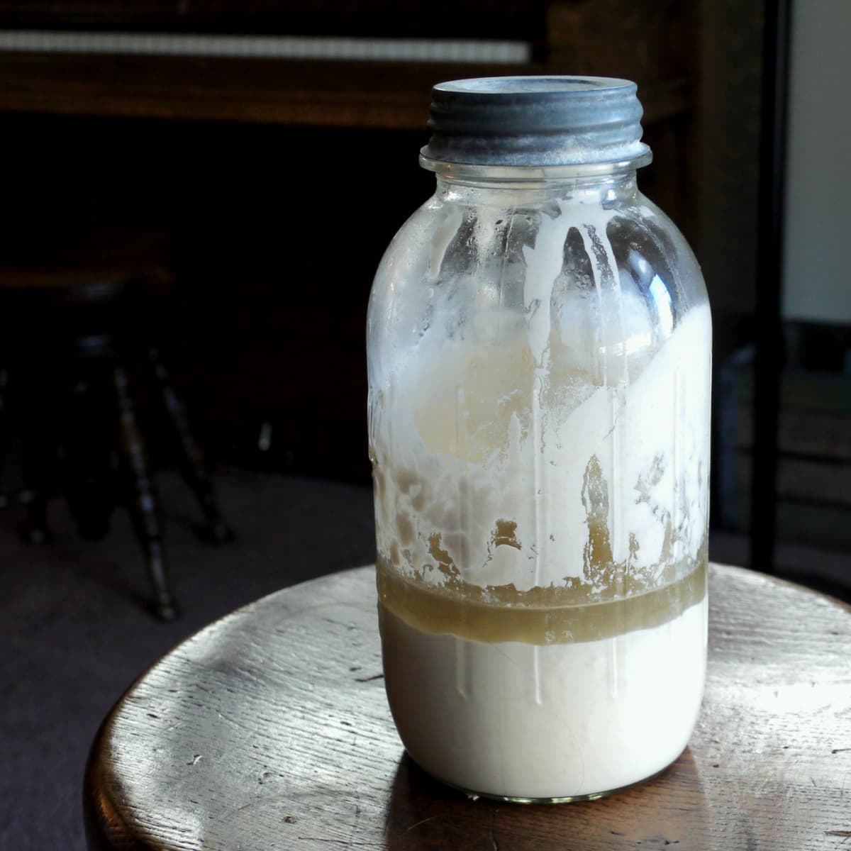 Large old Mason jar filled halfway with sourdough starter, with a half an inch of brownish hooch resting on top of the starter. 