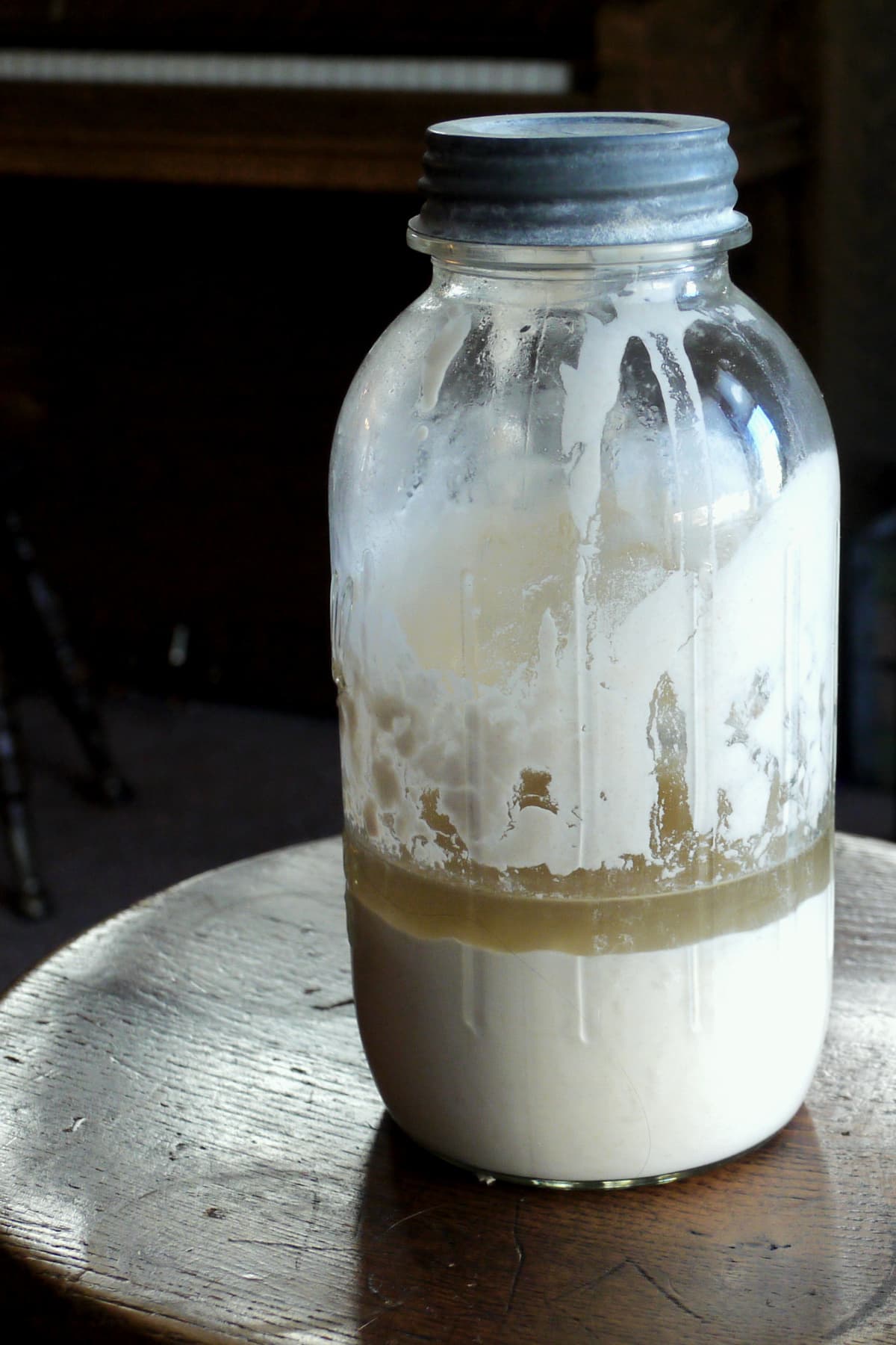 Large, tall old Mason jar filled halfway with sourdough starter, with a half an inch of brownish hooch resting on top of the starter. 