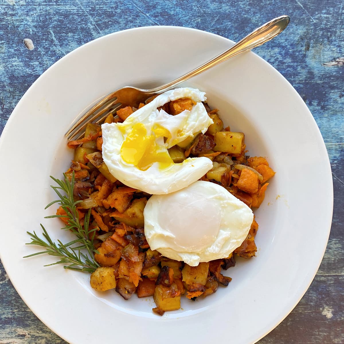 Overhead shot of a bowl of sweet potato hash with two poached eggs on top. One egg yolk is broken. 