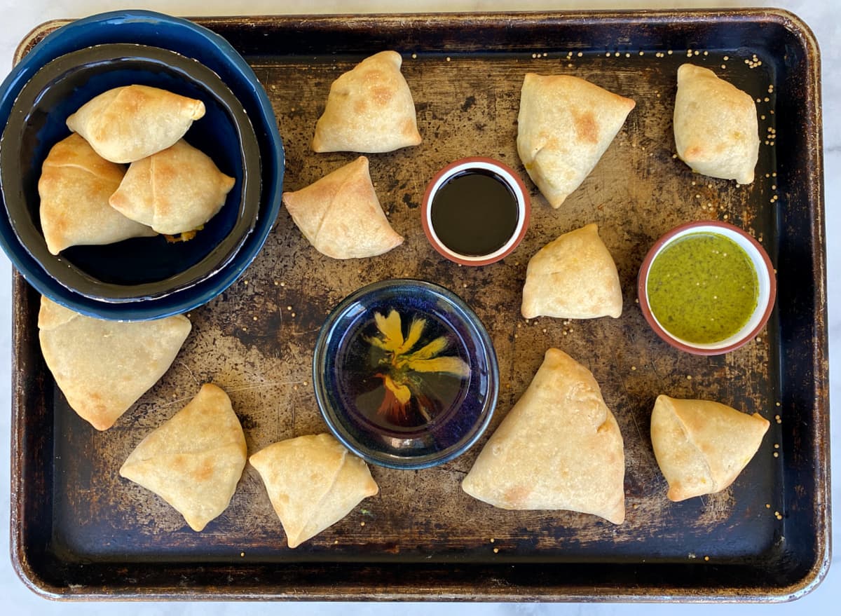 Sweet potato & butternut samosas on a tray with mint chutney, tamarind sauce, and Moosewood dipping sauce.