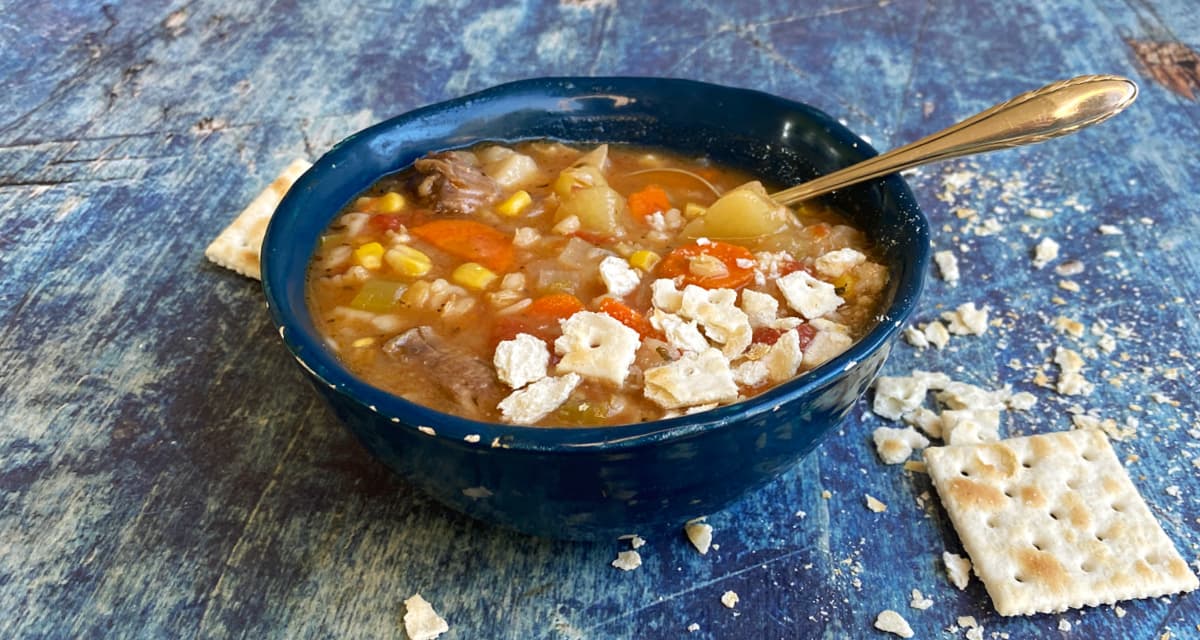 A bowl of vegetable soup, with crumbled saltine crackers sprinkled atop the soup.of the bowl.