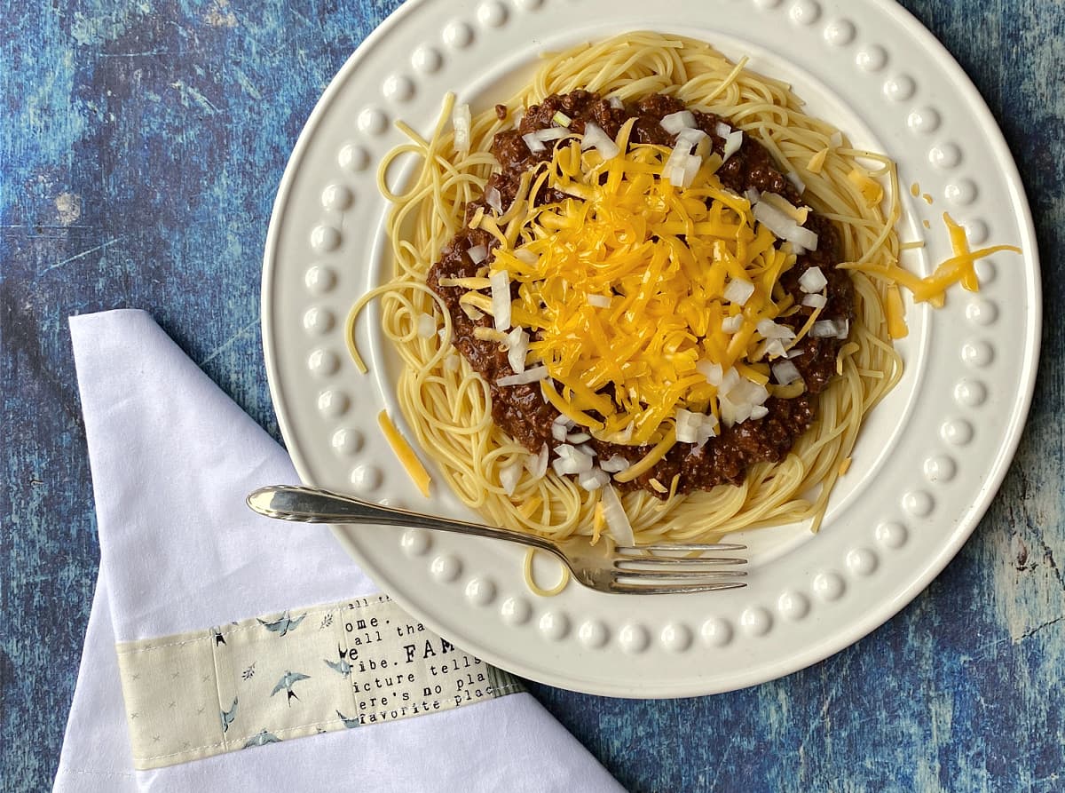 Chili and spaghetti, with fork on side of plate. White napkin on blue background. 