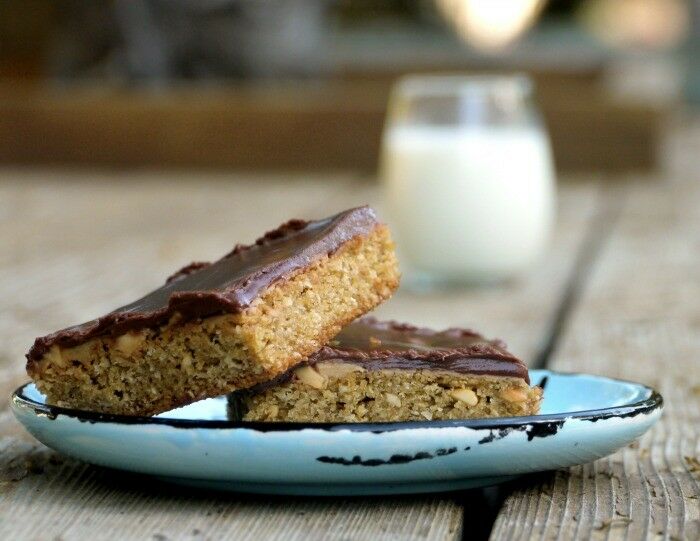 Close up of two chocolate topped bar cookies sitting on a small plate. Glass of milk is out of focus in the distance. 
