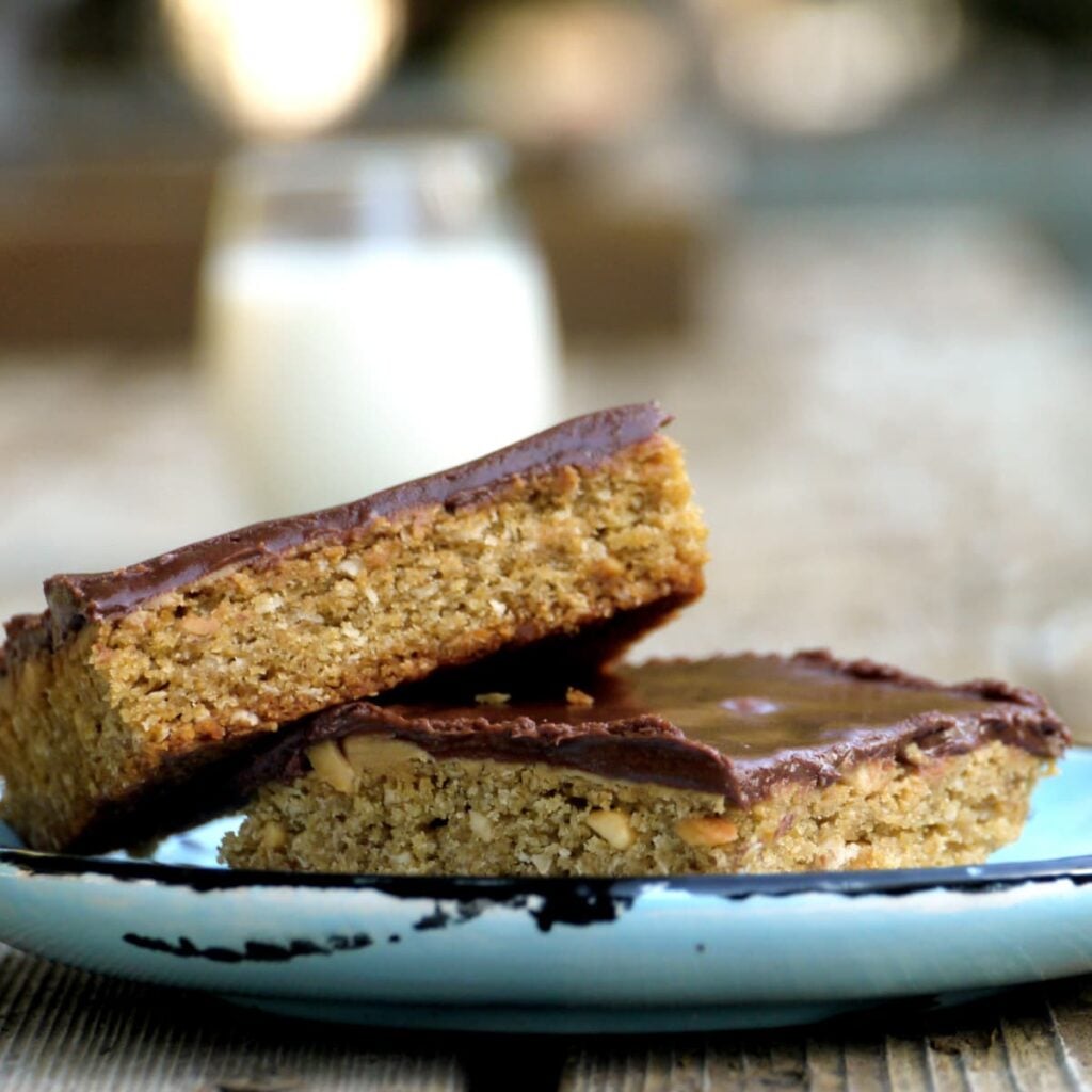 Two chocolate-frosted bar cookies on a plate. Glass of milk in background.