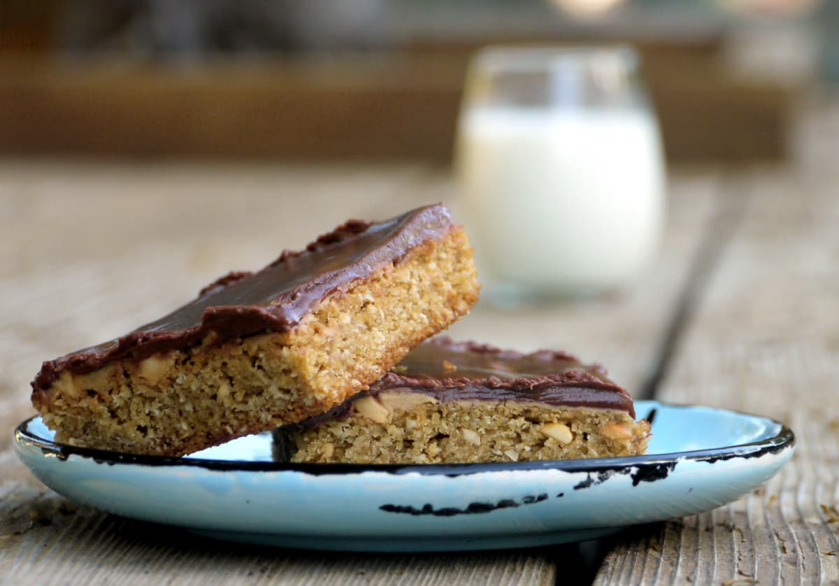 Two chocolate-frosted bar cookies on a plate. Glass of milk in background.