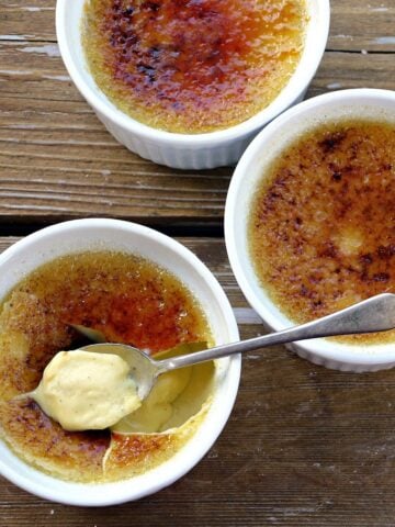 Three ramekins of creme brulee; one with the top cracked and a spoonful resting on top.