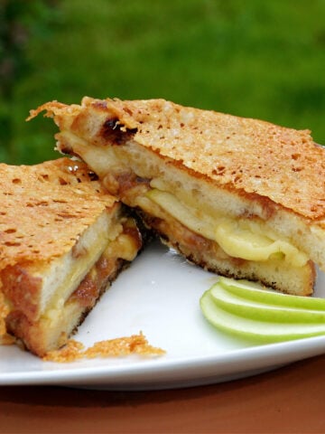 Grilled cheese sandwich, cut on diagonal, with cheese and apple butter smooshing out slightly. Three thin slices of granny smith apple fanned on the plate for garnish.