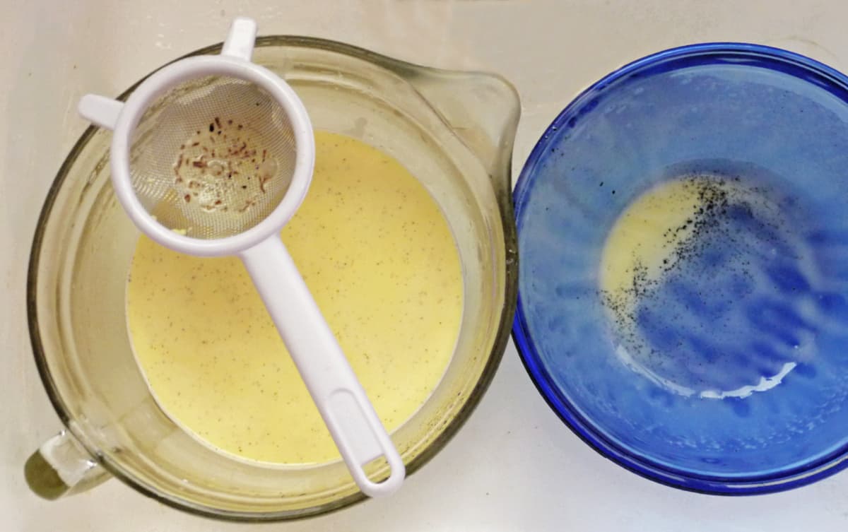 Two bowls: one empty with remnants of custard in bottom, the other with a small strainer resting above a bowl of strained custard.