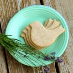Small plate with four bird-shaped shortbread cookies stacked on top. Fresh lavender on the side of the plate.