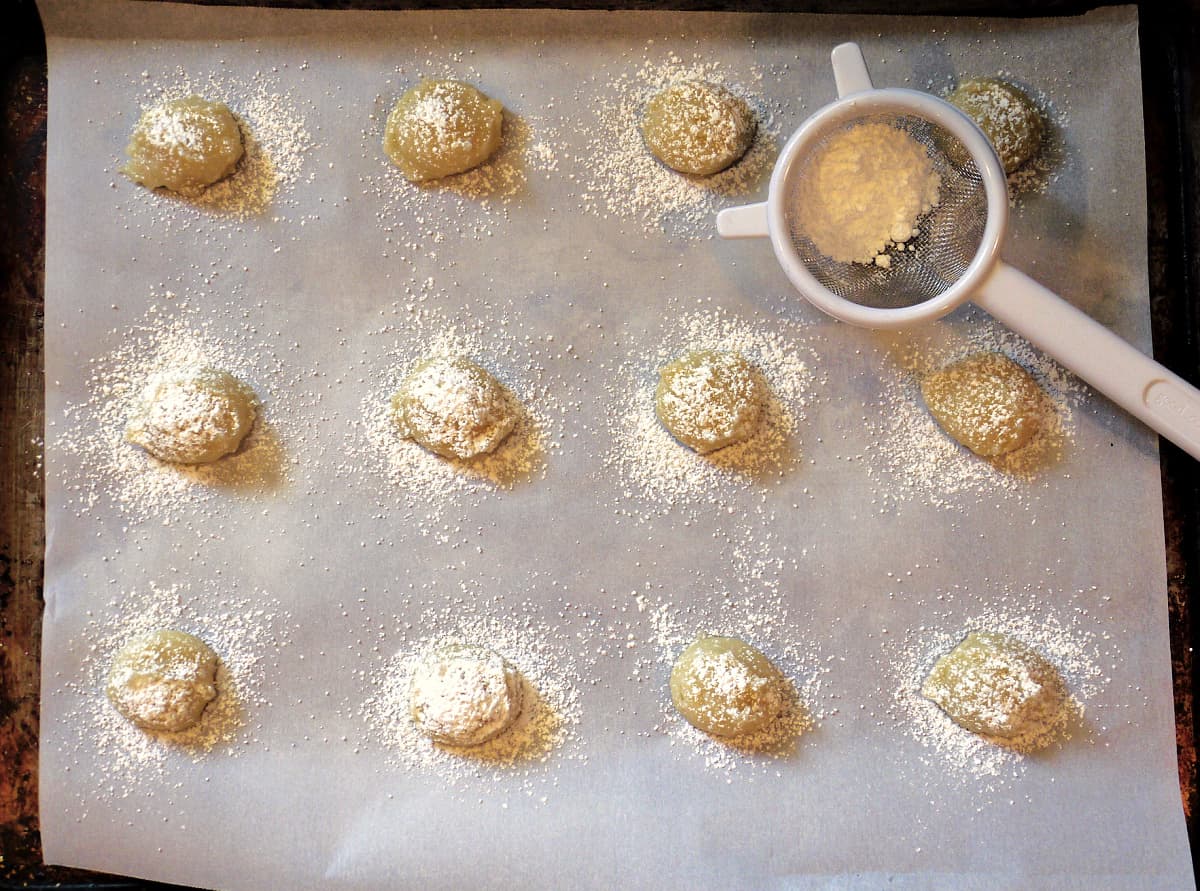Powdered sugar sprinkled onto scooped cookie dough on baking sheet.