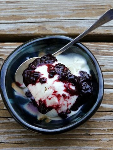 Overhead shot of vanilla ice cream in a small dish, with berry compote poured over the top.