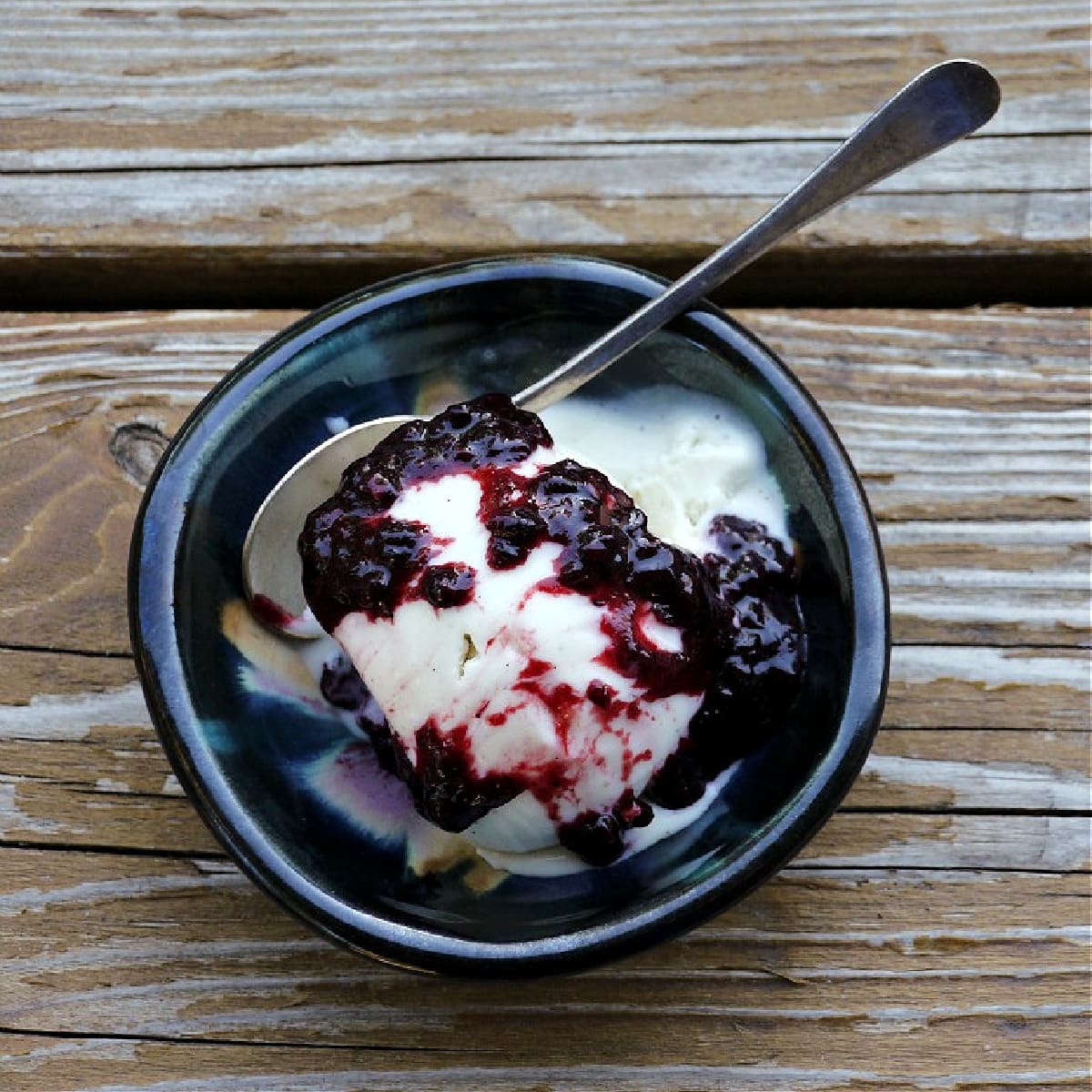 Overhead shot of vanilla ice cream in a small dish, with berry compote poured over the top.