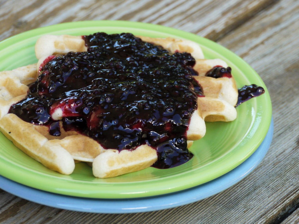 Two stacked plates with a waffle topped with blackberry compote. 