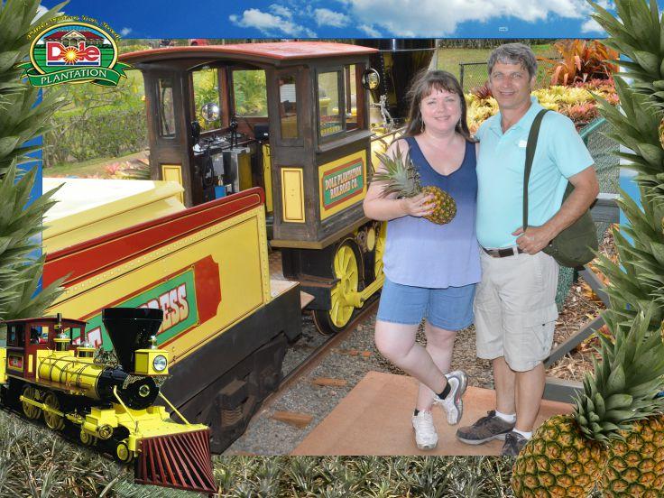 Couple with small pineapple posing in front of Pineapple Express small-guage train. 