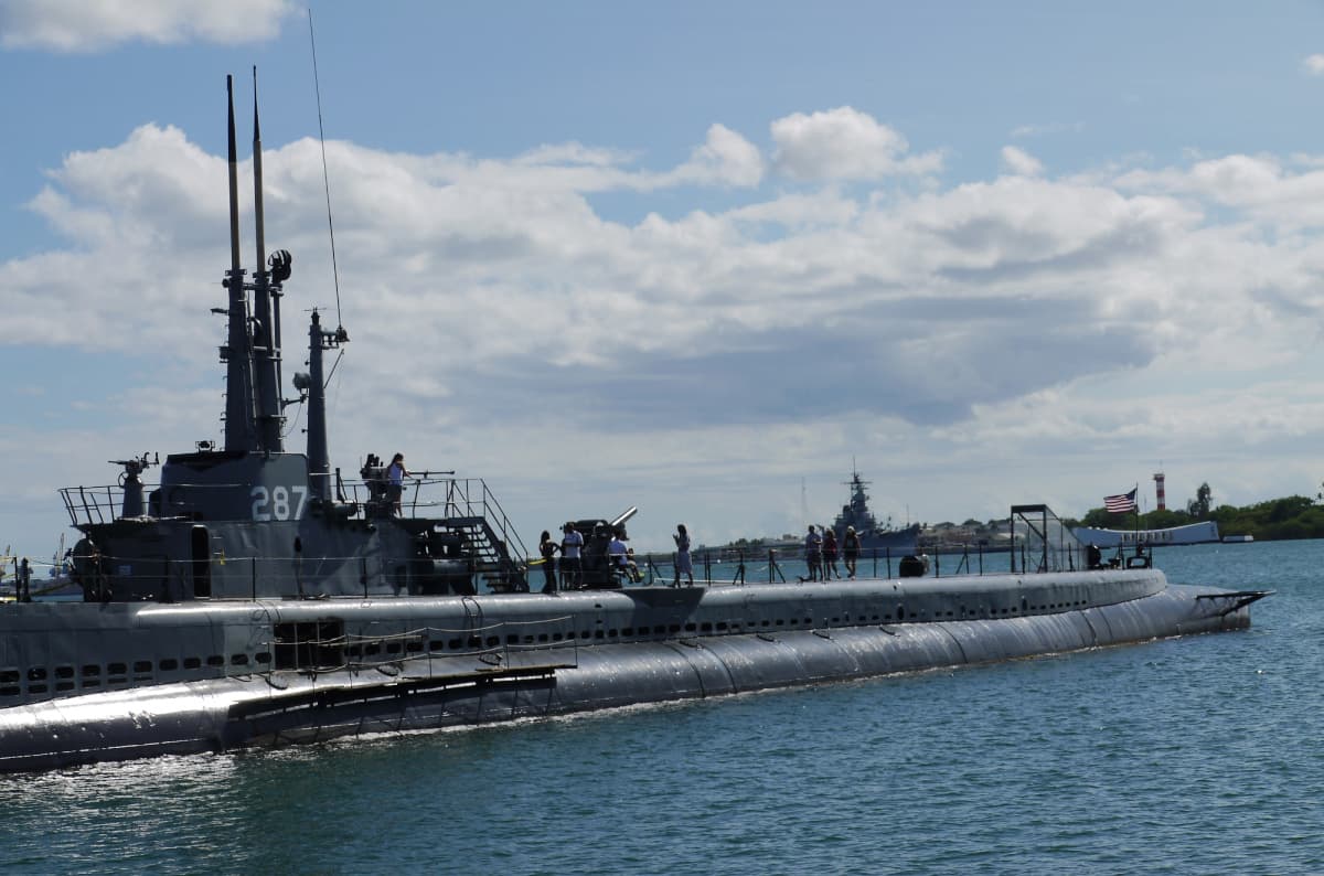 USS Bowfin surfaced in Pearl Harbor, with tourists walking around on deck.