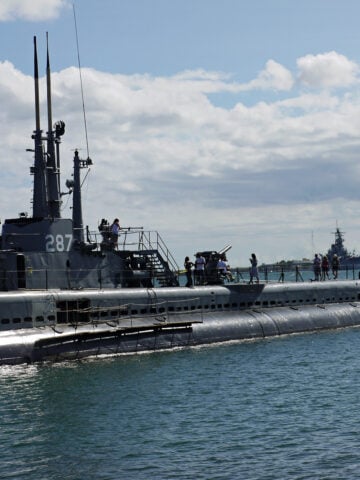 USS Bowfin surfaced in Pearl Harbor, with tourists walking around on deck.