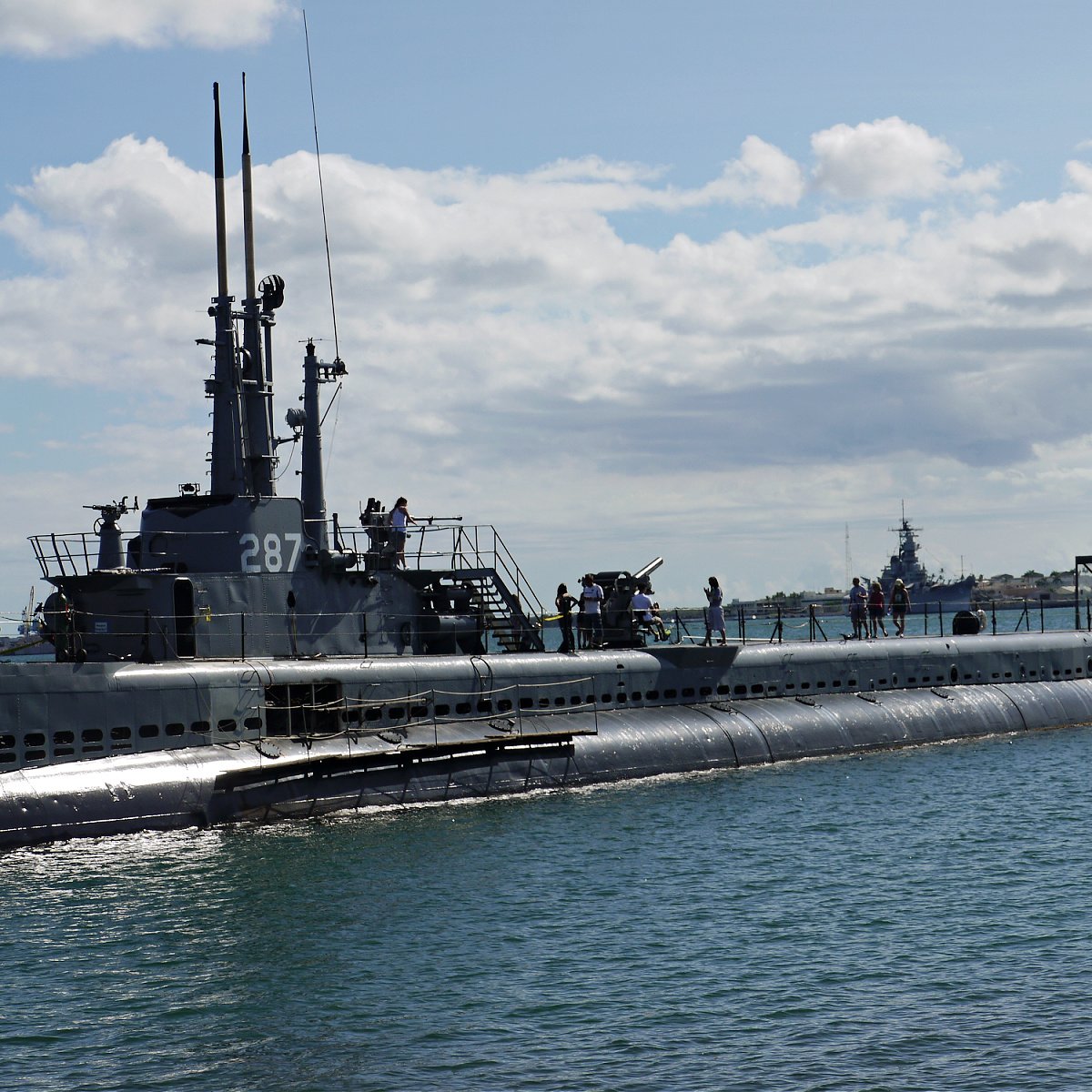 USS Bowfin surfaced in Pearl Harbor, with tourists walking around on deck.