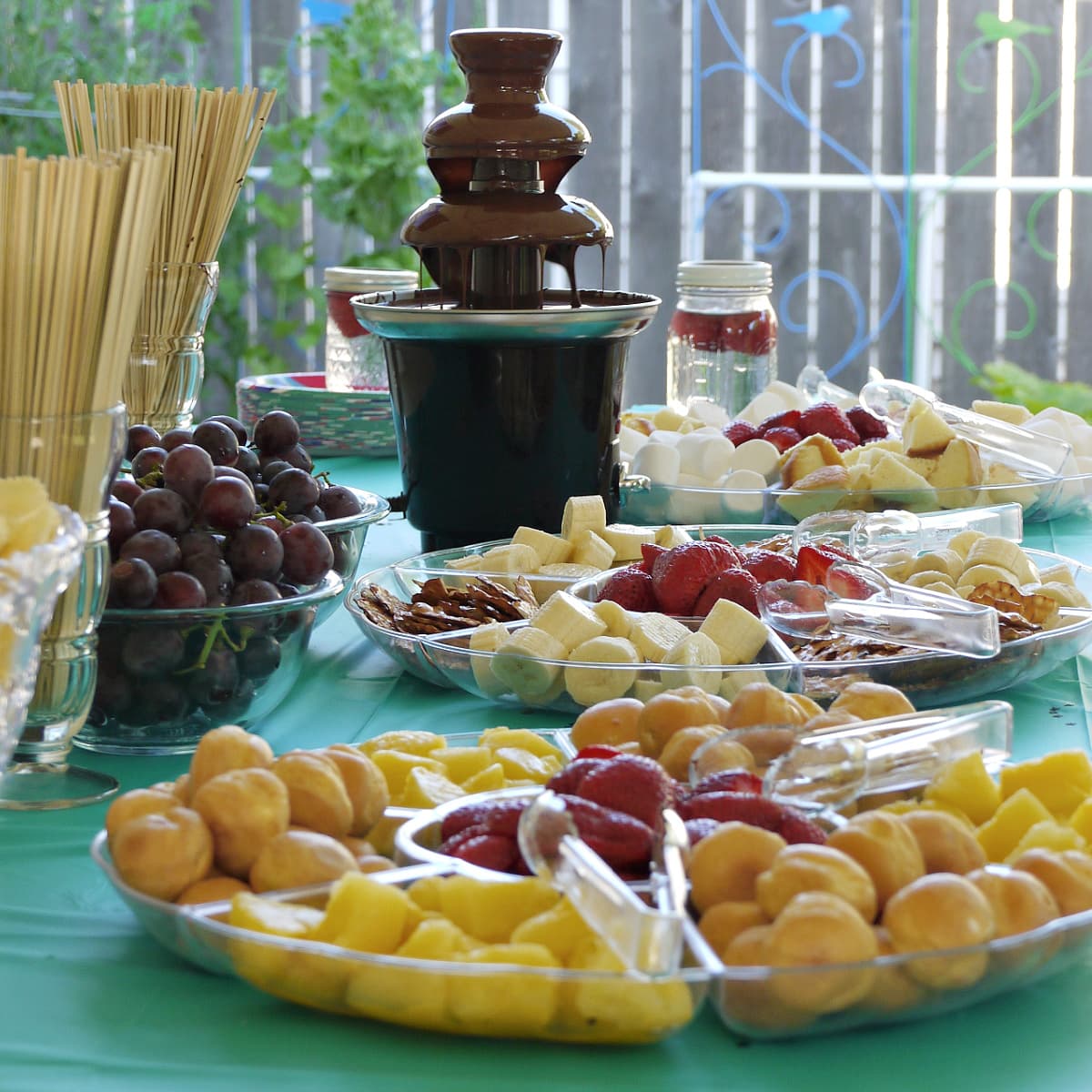 Table set with plates full of dippers, with a chocolate fountain flowing in the background. 