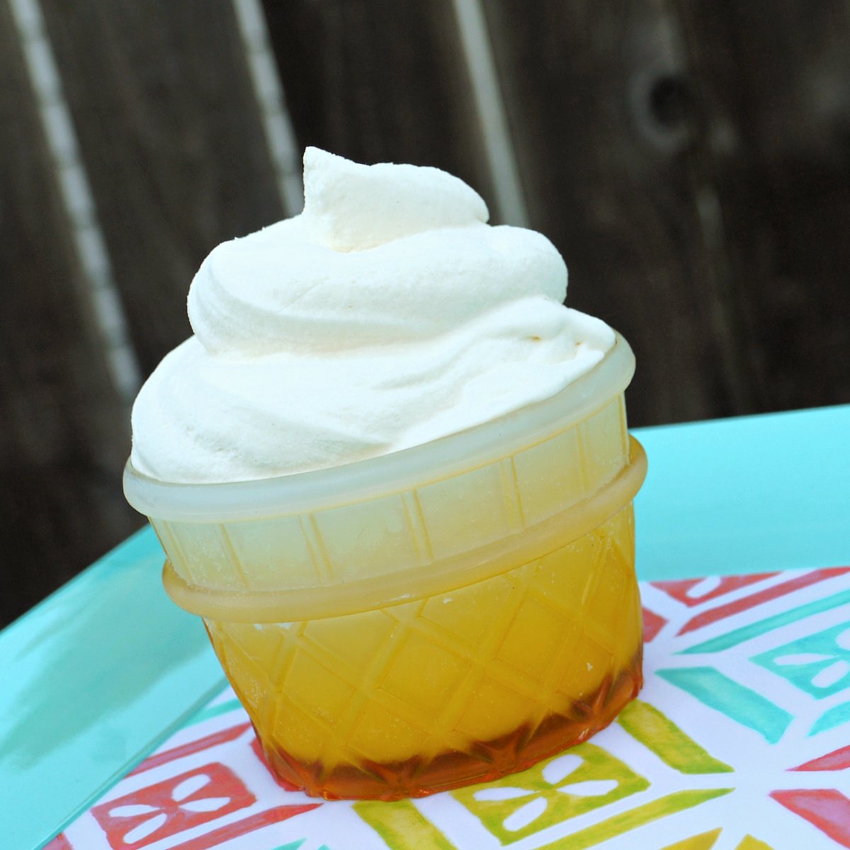 Closeup of some copycat Dole Whip soft serve in an ice cream cone-shaped bowl of a summery square serving tray. 
