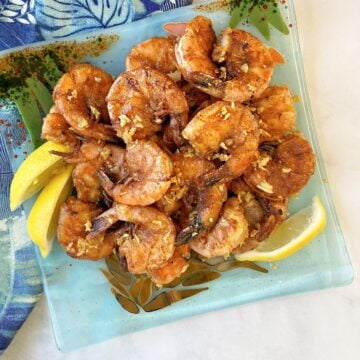 Overhead shot of a plate of garlic shrimp, garnished with lemon slices. Hawaiian fabric in background.