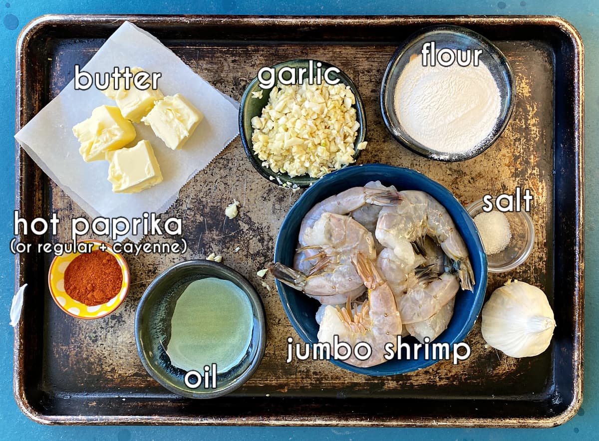 Ingredients for garlic shrimp, displayed on old sheet pan: garlic, butter, shrimp, flour, paprika, oil, salt.