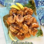 Plate of garlic shrimp, garnished with lemon slices. Hawaiian fabric in background. Pin text reads: Hawaiian Garlic Shrimp (Kahuku Shrimp Truck-style)