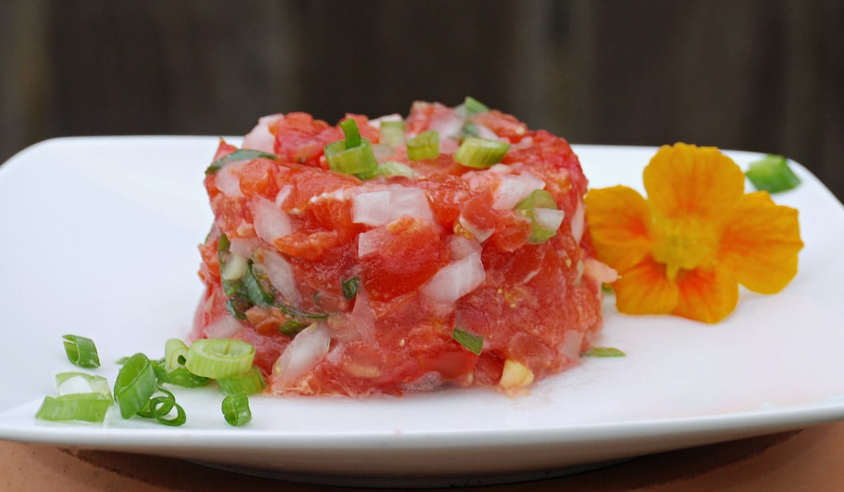 Serving of lomi salmon on a plate, garnished with additonal green onions and nasturtiums.