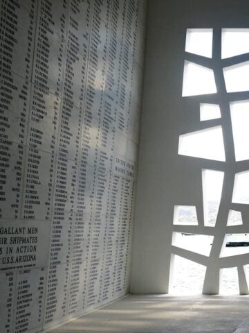 Interior of the Shine Room at the Arizona Memorial, with sunlight coming through the cut out pattern on the side. Names engraved on the wall to the left go from floor to ceiling.