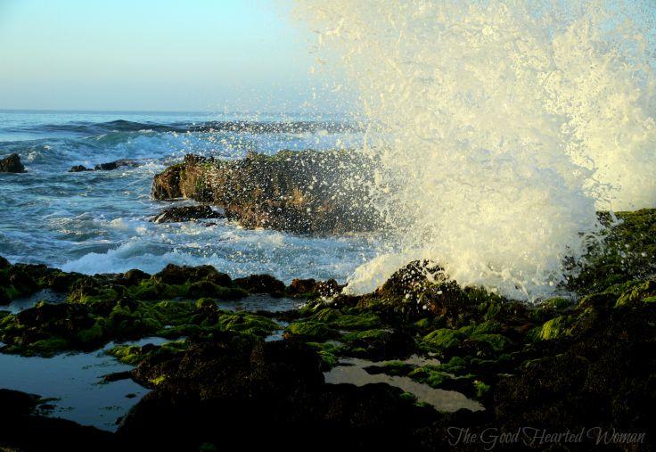Sunlit water splashing against rocks in foreground' ocean beyond. 