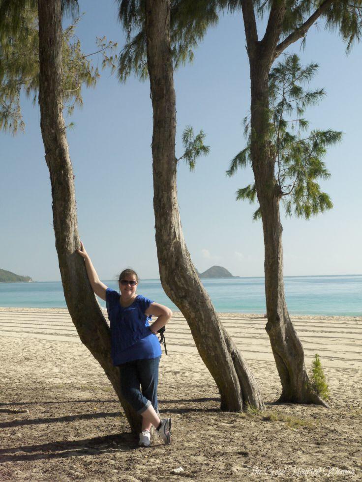 Woman in tennis shoes leaning against a curved tree trunk.