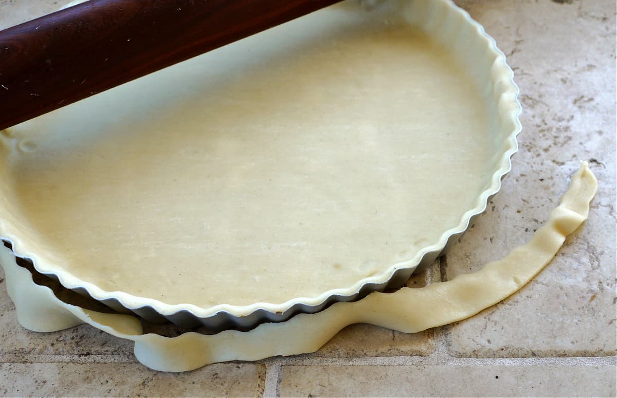 Unbaked pastry crust rolled into a tart pan. The rolling pin has partially trimmed the edges.