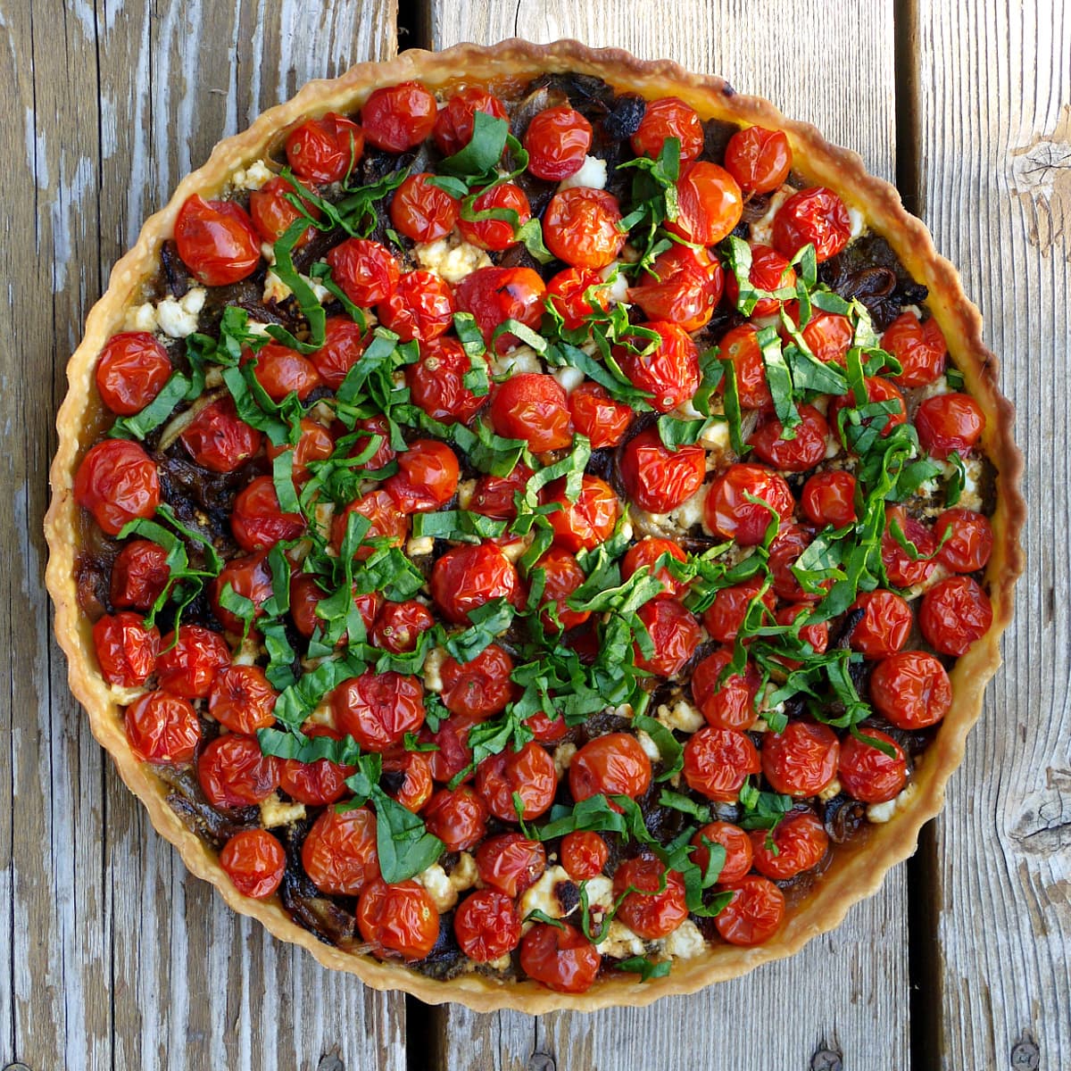 Overhead shot of fresh cherry tomato tart, baked and garnished with fresh spinach ribbons.