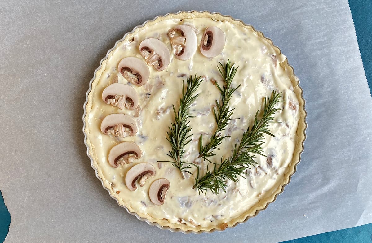 Tart decorated with mushroom slices and rosemary sprigs, read to go in the oven.