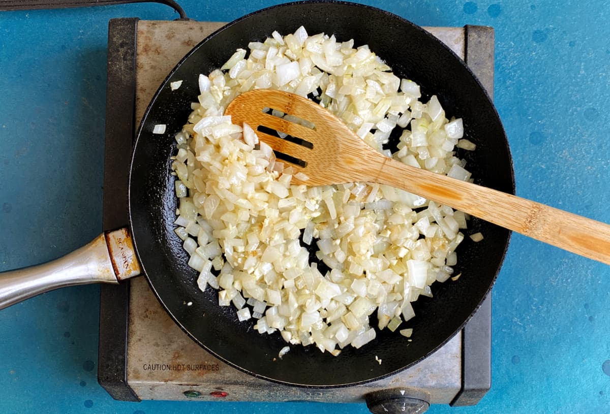 Sauteed onions and garlic in a medium skillet, with a slotted wooden spoon in the mix.