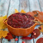 Pumpkin-shaped dish with top removed, filled with prepared cranberry sauce. Pin text reads: Orange SPiced Cranberry Sauce | Quck & Easy 20-minute prep.