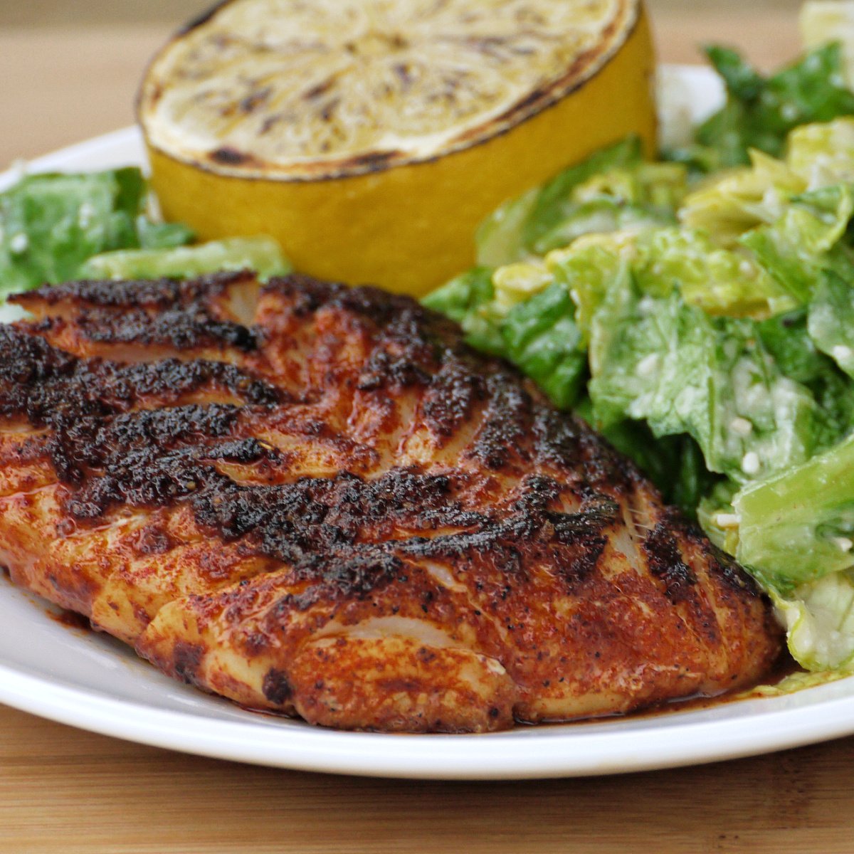Spicy Pan-fried Blackened Rockfish, plated with a green salad and a grilled lemon.