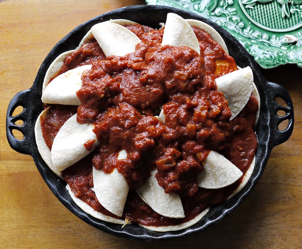 Small enchiladas arranged as spokes in wheel in pie dish, topped with thick red sauce.
