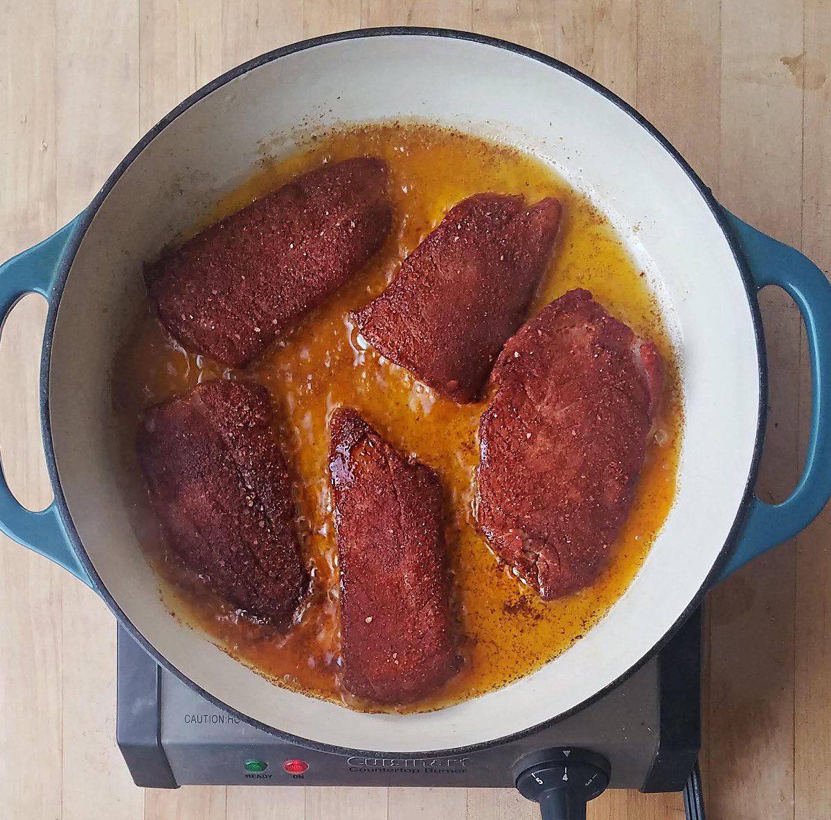Five dry-rubbed fillets cooking in a large enamel-lined cast iron skillet. 