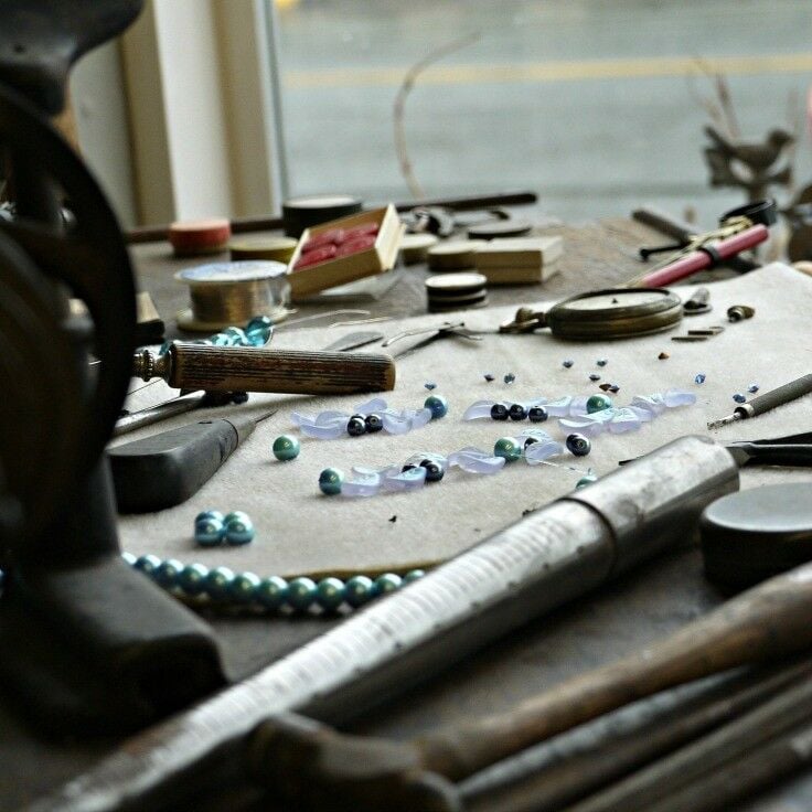Front window display of Elisabeth's by the Sea; teal pearls and jewelry making tools on a wooden work surface. 