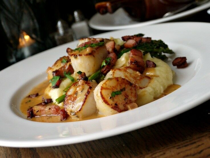 Pan-seared Alaskan Scallops on a white plate, garnished with parsley and a thin white wine sauce. 