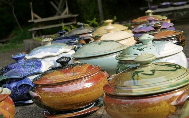 Many clay casserole pots of various colors on display on wooden table at Orcas Island Pottery.