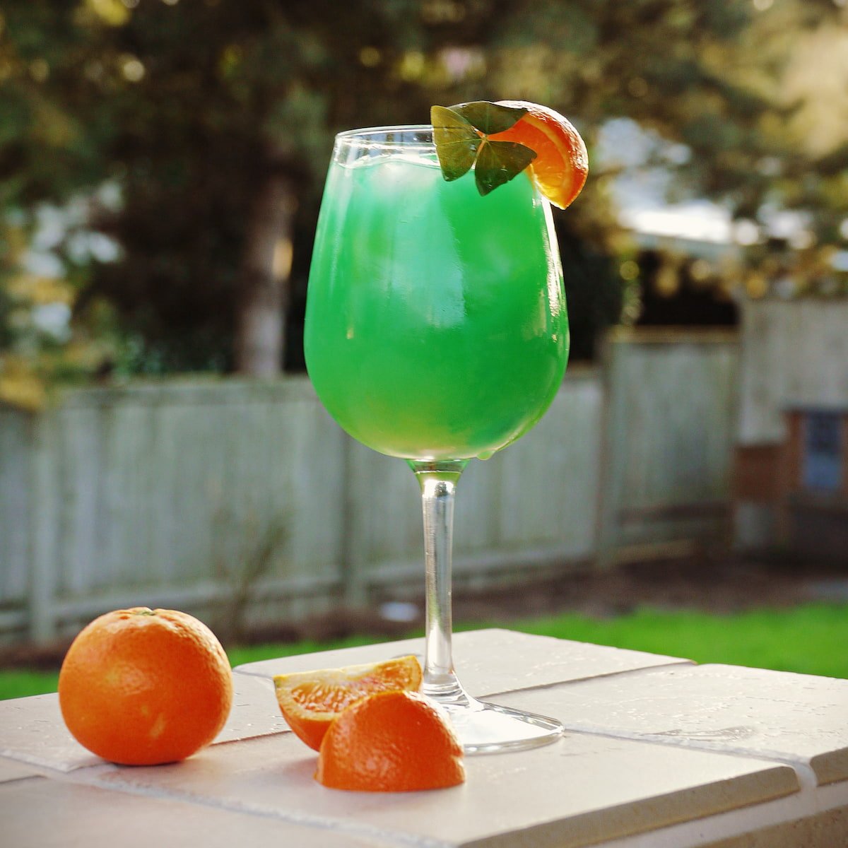 Green mixed drink in a wine glas, garnished with an orange slice and a shamrock.
