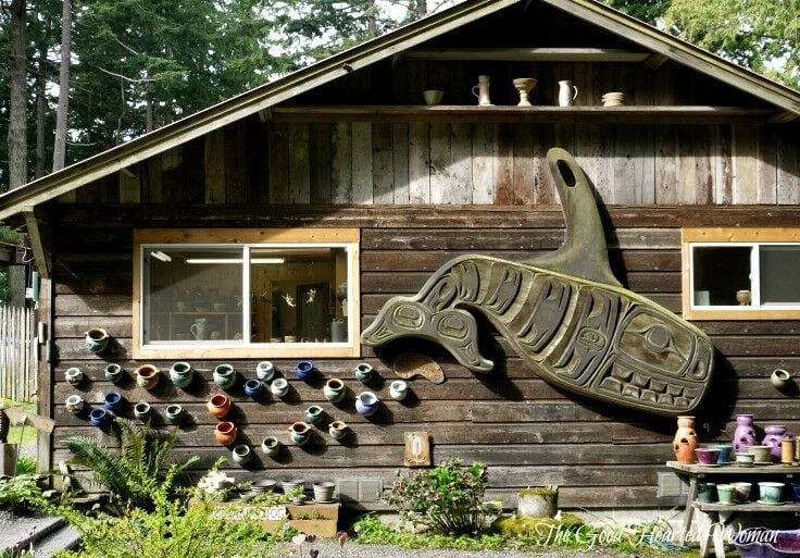 Side view of exterior of pottery shed, with large carved wooden Pacific NW native whale mounted on the side, and many wall pots also.  