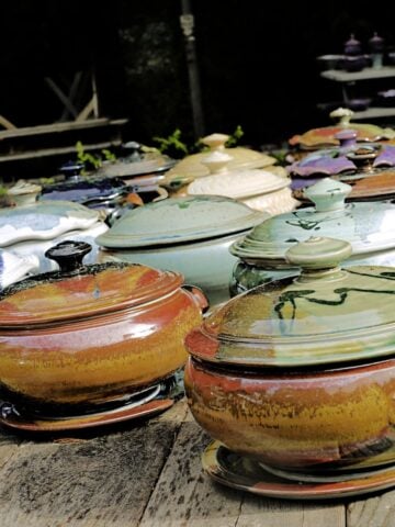 Colorful clay casserole pots with lids, setting at angle on wooden table.