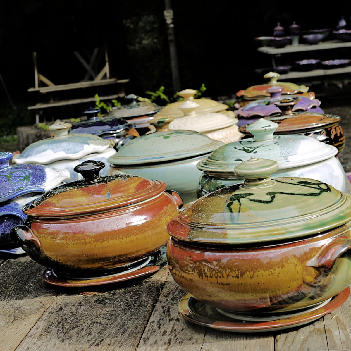 Colorful clay casserole pots with lids, setting at angle on wooden table. 